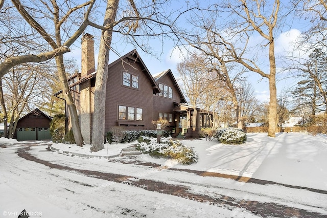 view of snowy exterior featuring an outbuilding, a chimney, and a garage