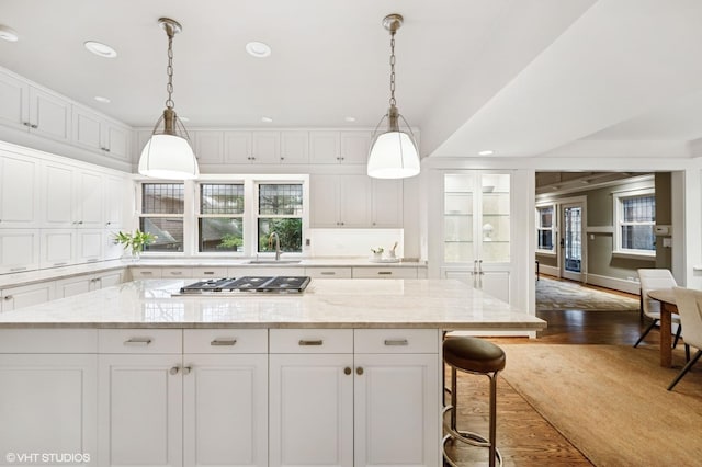 kitchen with a center island, stainless steel gas stovetop, dark wood-style floors, white cabinets, and a sink