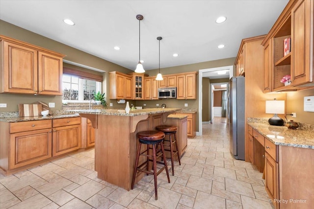 kitchen with light stone countertops, recessed lighting, appliances with stainless steel finishes, a center island, and a kitchen bar