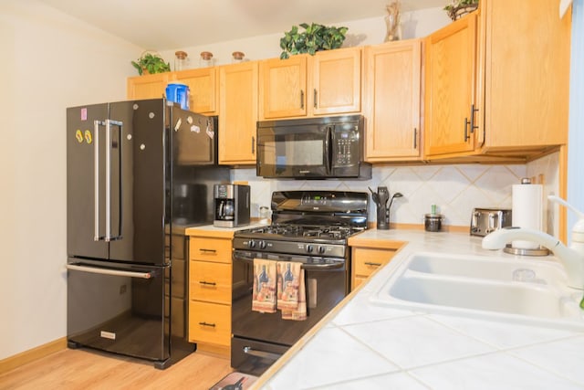 kitchen featuring sink, black appliances, decorative backsplash, tile countertops, and light brown cabinets