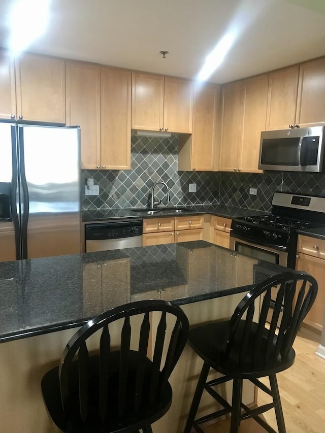 kitchen featuring sink, light hardwood / wood-style flooring, light brown cabinets, dark stone countertops, and appliances with stainless steel finishes