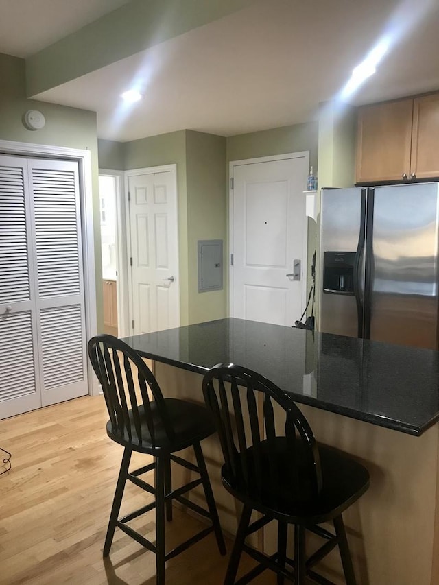 kitchen featuring stainless steel fridge with ice dispenser, light hardwood / wood-style floors, a breakfast bar, and dark stone counters