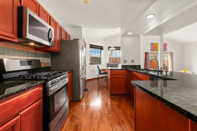 kitchen featuring stainless steel appliances, a sink, vaulted ceiling, backsplash, and dark wood-style floors