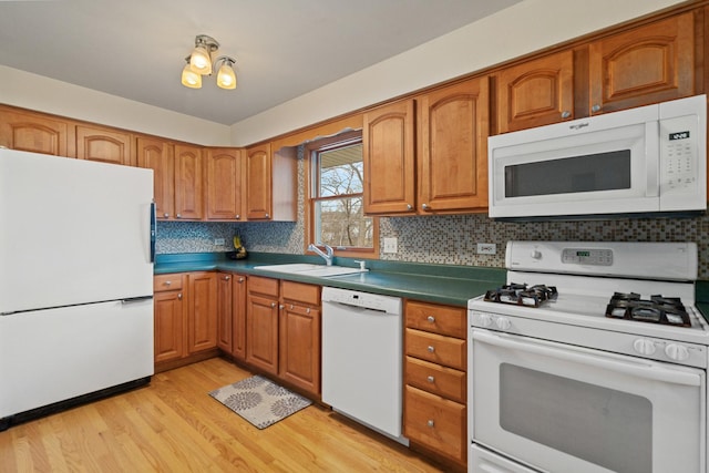 kitchen featuring light wood finished floors, white appliances, a sink, and brown cabinets