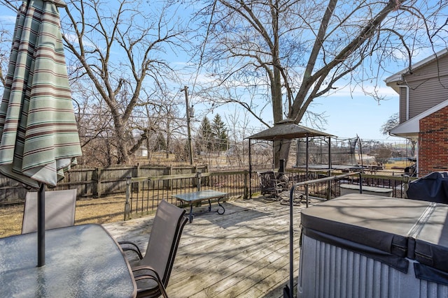 wooden deck featuring a trampoline, outdoor dining space, and fence