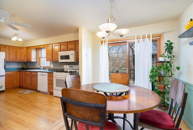 kitchen with white appliances, a sink, decorative backsplash, light wood finished floors, and dark countertops