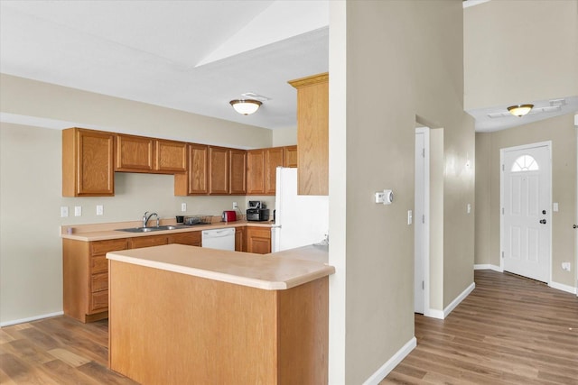 kitchen featuring lofted ceiling, sink, white appliances, kitchen peninsula, and light wood-type flooring