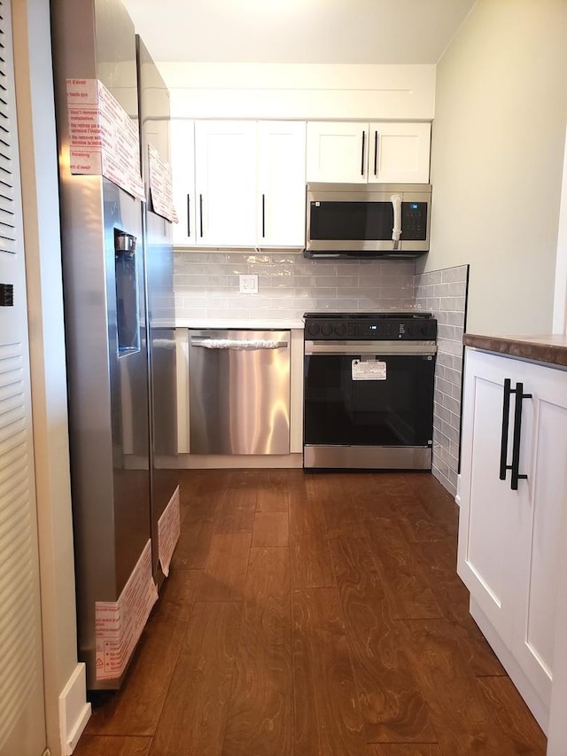 kitchen with appliances with stainless steel finishes, dark hardwood / wood-style flooring, white cabinetry, and backsplash