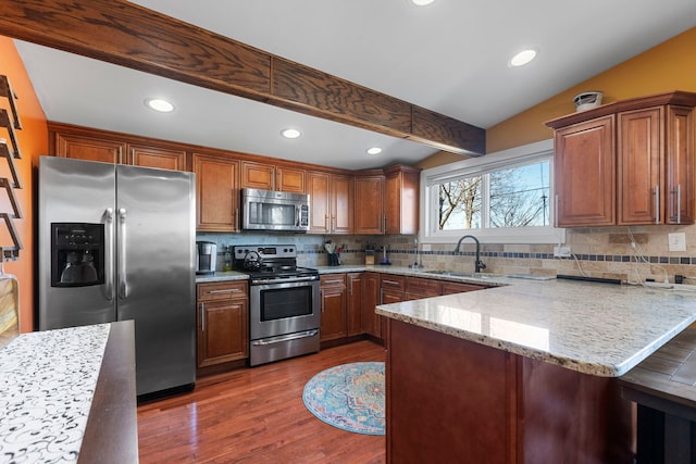 kitchen with a peninsula, dark wood-style flooring, a sink, appliances with stainless steel finishes, and light stone countertops