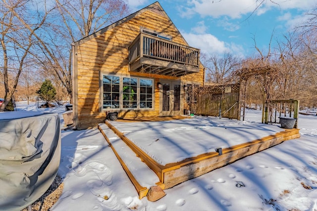 snow covered house featuring a balcony and fence