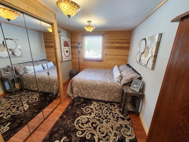 bedroom with crown molding, light wood finished floors, baseboards, and wooden walls