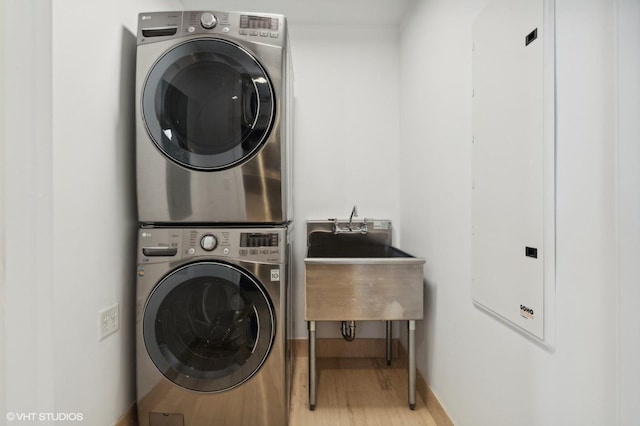 clothes washing area featuring stacked washer / dryer, sink, and light hardwood / wood-style floors