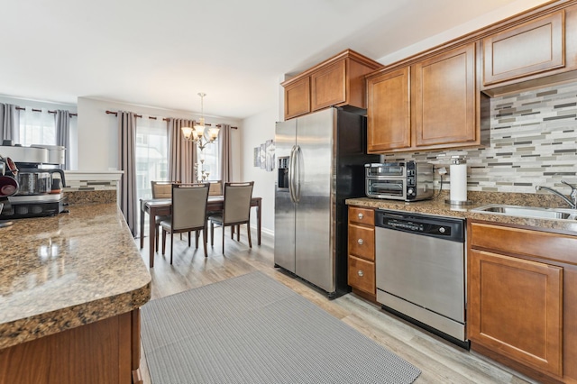 kitchen featuring stainless steel appliances, a sink, tasteful backsplash, brown cabinetry, and decorative light fixtures