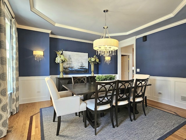 dining room featuring an inviting chandelier, wood-type flooring, ornamental molding, and a raised ceiling