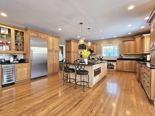 kitchen featuring hanging light fixtures, a center island, built in appliances, beverage cooler, and light wood-type flooring