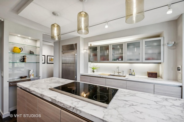 kitchen featuring sink, black electric cooktop, built in refrigerator, light stone counters, and pendant lighting