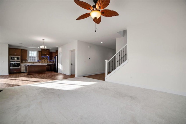 unfurnished living room featuring ceiling fan with notable chandelier and dark colored carpet