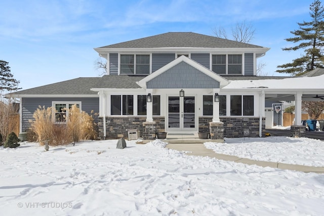 snow covered back of property featuring a shingled roof and stone siding