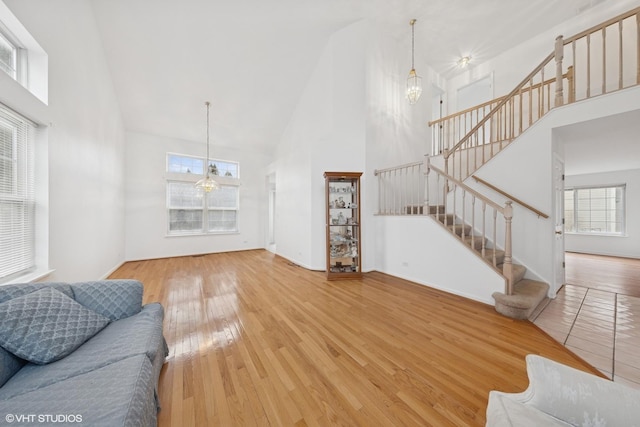 living area with a towering ceiling, stairs, an inviting chandelier, and hardwood / wood-style flooring