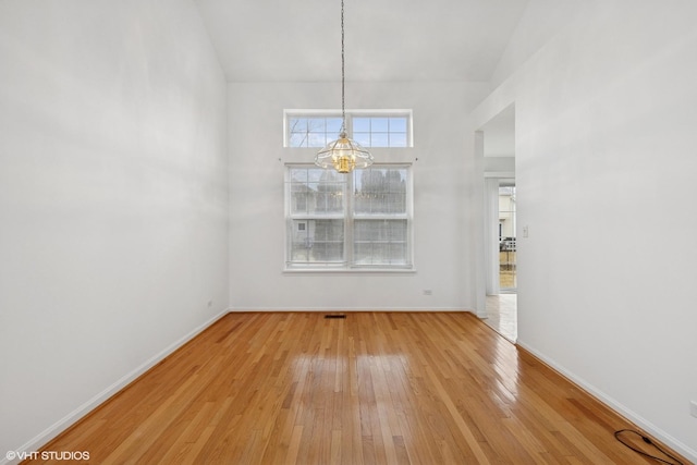 unfurnished dining area featuring a chandelier, light wood-style flooring, and baseboards