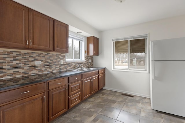 kitchen featuring sink, dark stone countertops, dark tile patterned flooring, white fridge, and decorative backsplash