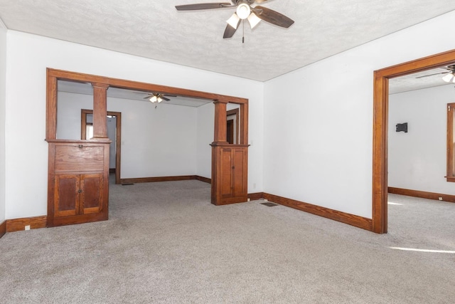 carpeted empty room with ornate columns, ceiling fan, and a textured ceiling