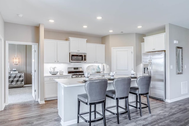 kitchen with appliances with stainless steel finishes, an island with sink, a breakfast bar area, white cabinets, and decorative backsplash