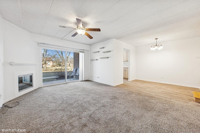 unfurnished living room with ceiling fan with notable chandelier, a textured ceiling, a glass covered fireplace, baseboards, and light colored carpet