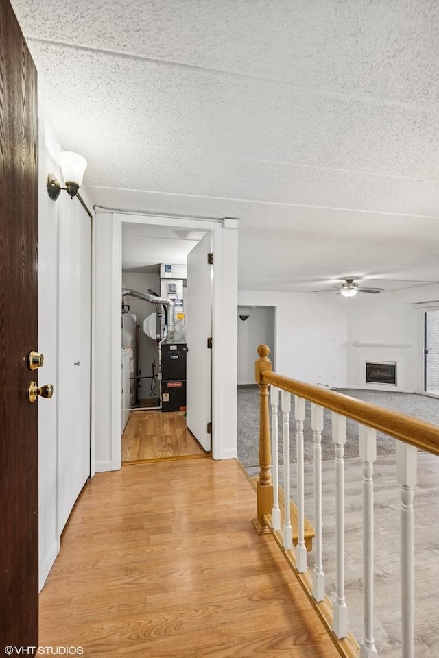 hall with light wood-type flooring, an upstairs landing, heating unit, a textured ceiling, and water heater