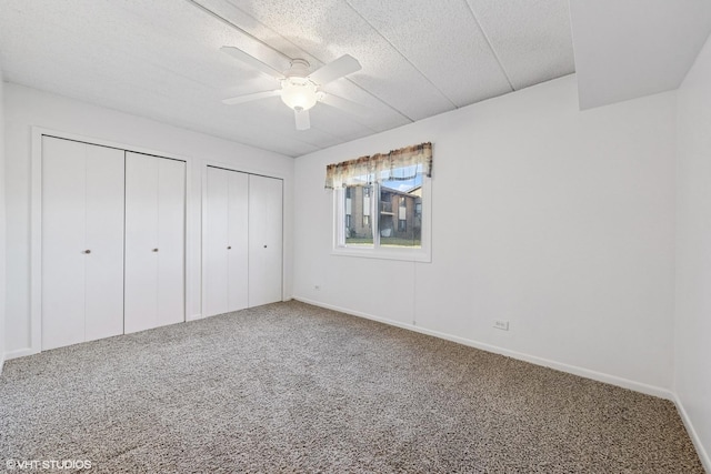 unfurnished bedroom featuring carpet, baseboards, ceiling fan, a textured ceiling, and two closets