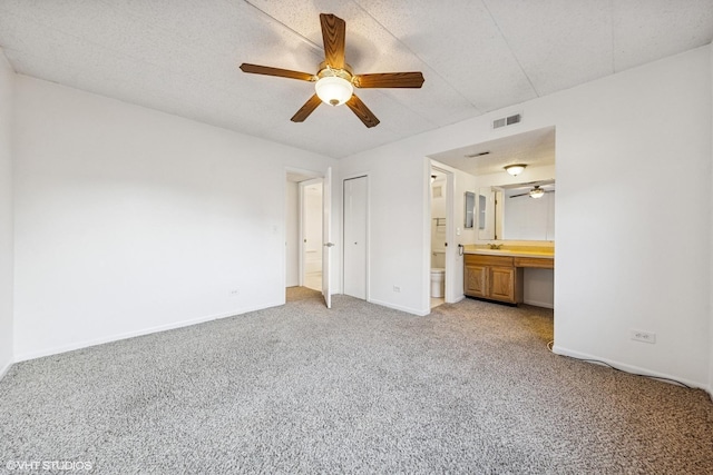 unfurnished bedroom with visible vents, connected bathroom, baseboards, light colored carpet, and built in desk