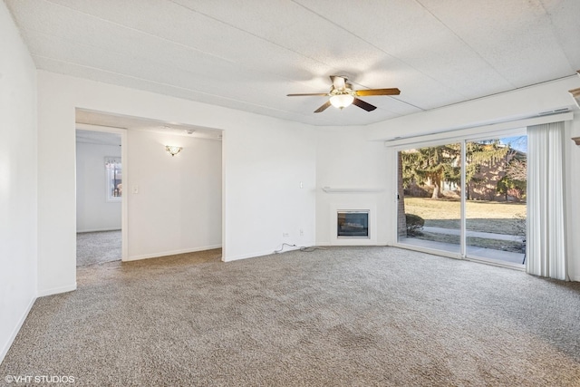 unfurnished living room featuring a glass covered fireplace, ceiling fan, baseboards, and carpet