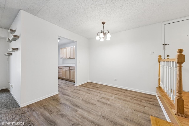 unfurnished dining area with light wood finished floors, a textured ceiling, baseboards, and an inviting chandelier