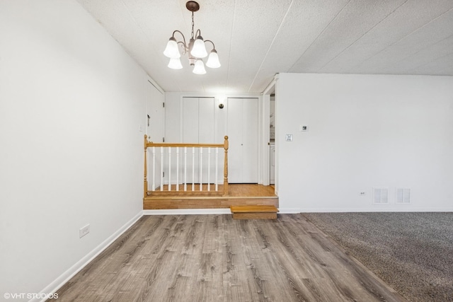 empty room featuring visible vents, baseboards, a notable chandelier, and wood finished floors