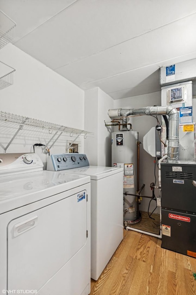 laundry room with washer and clothes dryer, heating unit, water heater, light wood finished floors, and laundry area