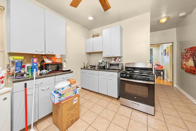 kitchen featuring stainless steel gas range oven, white cabinets, ceiling fan, light tile patterned flooring, and fridge