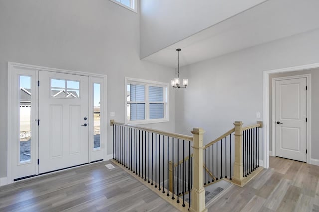 foyer entrance featuring baseboards, a high ceiling, wood finished floors, and a notable chandelier