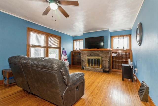 living area featuring light wood-style floors, a brick fireplace, a healthy amount of sunlight, and ornamental molding