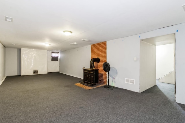 finished below grade area featuring visible vents, dark carpet, and a wood stove