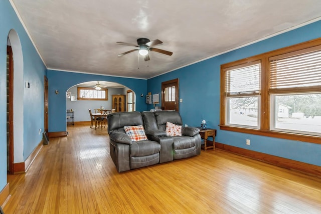 living area with arched walkways, crown molding, hardwood / wood-style floors, ceiling fan, and baseboards