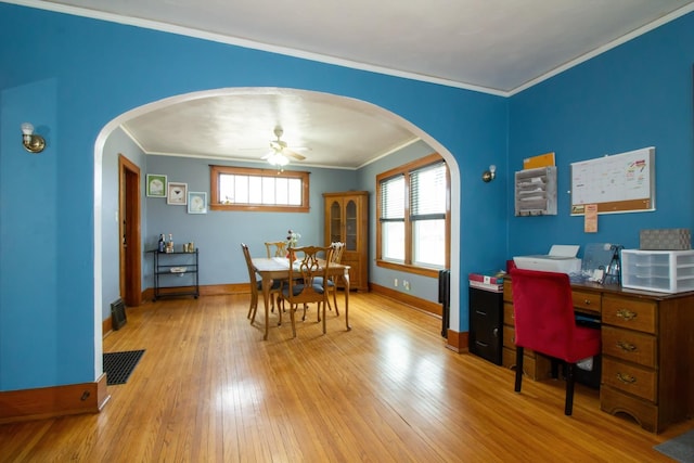 dining space featuring arched walkways, a ceiling fan, baseboards, light wood finished floors, and crown molding