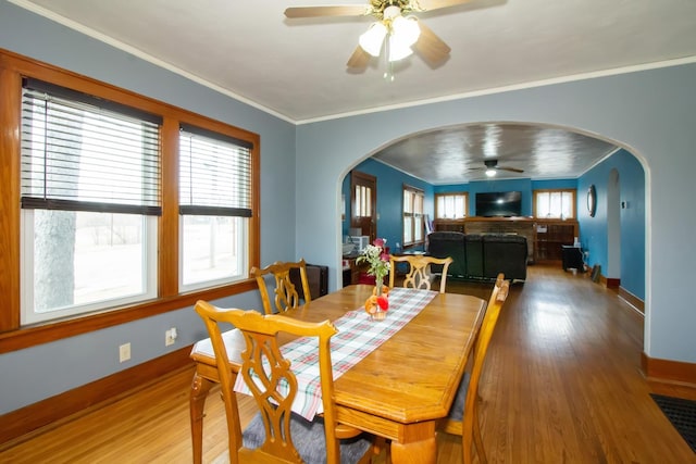 dining space with baseboards, arched walkways, wood finished floors, and ornamental molding