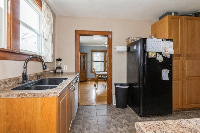 kitchen with brown cabinets, light countertops, freestanding refrigerator, a sink, and dishwasher