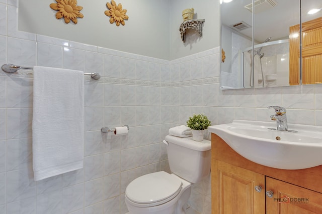 bathroom featuring vanity, toilet, a shower with shower door, and tile walls