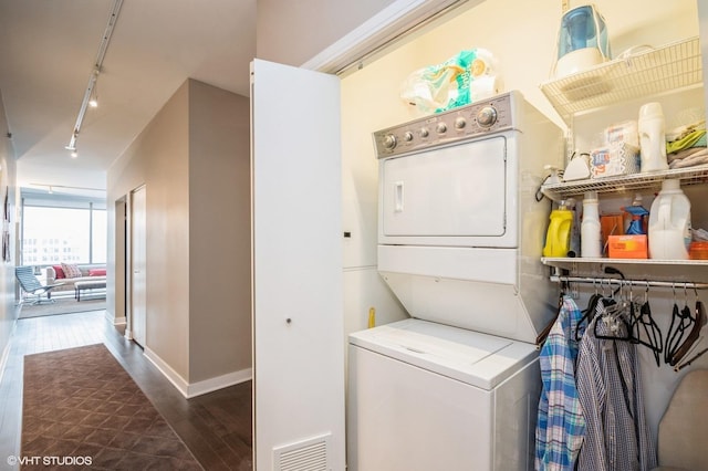 clothes washing area featuring dark hardwood / wood-style flooring, track lighting, and stacked washer / drying machine