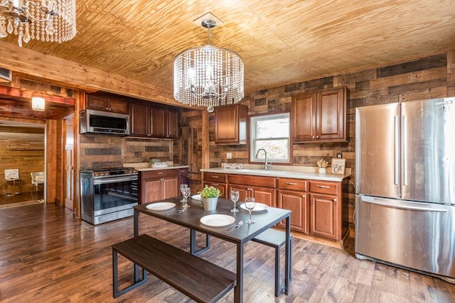 kitchen with an inviting chandelier, appliances with stainless steel finishes, light wood-type flooring, and pendant lighting