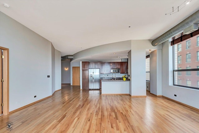 unfurnished living room featuring baseboards, a sink, and light wood-style floors