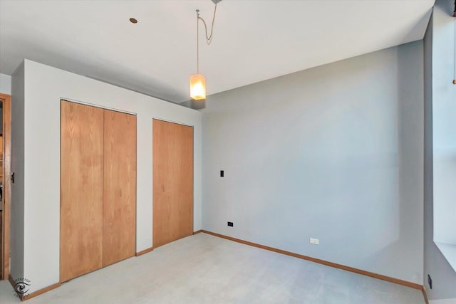 unfurnished bedroom featuring baseboards, two closets, and light colored carpet