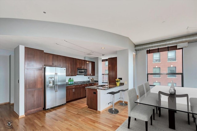 kitchen featuring a breakfast bar area, light wood-style flooring, stainless steel appliances, a peninsula, and a sink