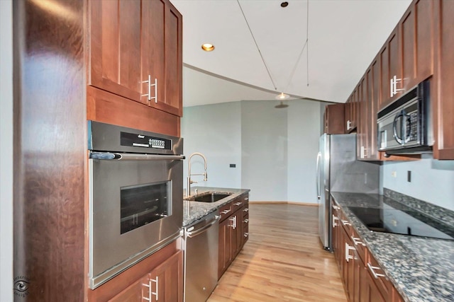 kitchen with recessed lighting, appliances with stainless steel finishes, a sink, dark stone countertops, and light wood-type flooring